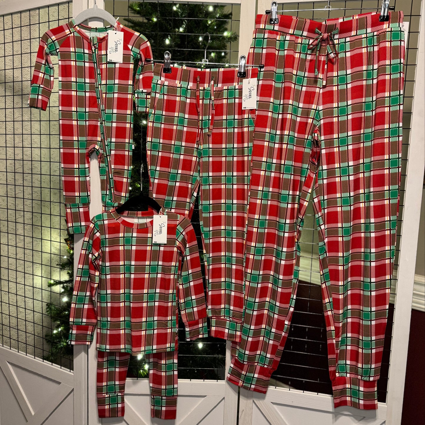 Plaid you're here family pajamas hanging in front of a Christmas tree.