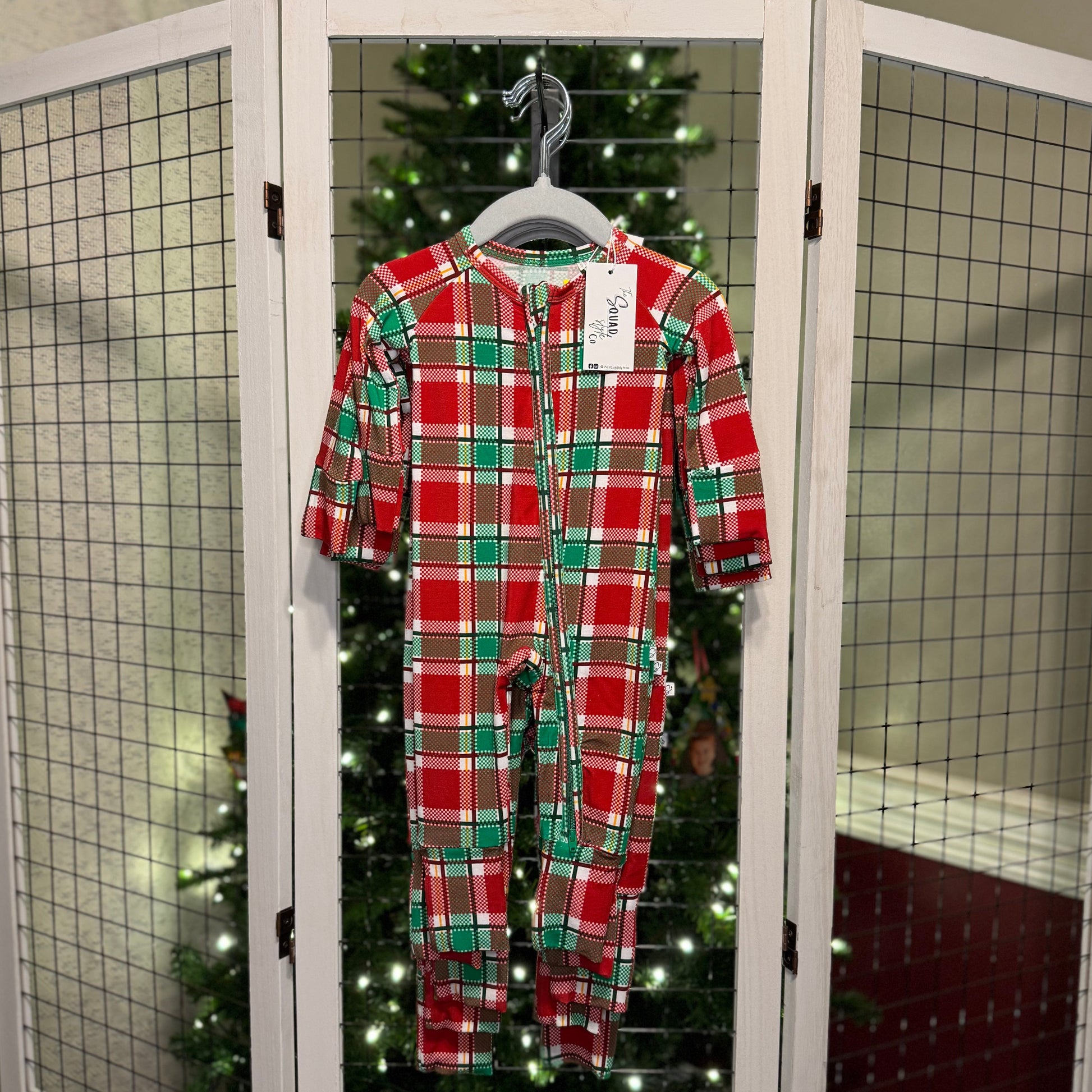 Plaid you're here convertible romper hanging in front of a Christmas tree.
