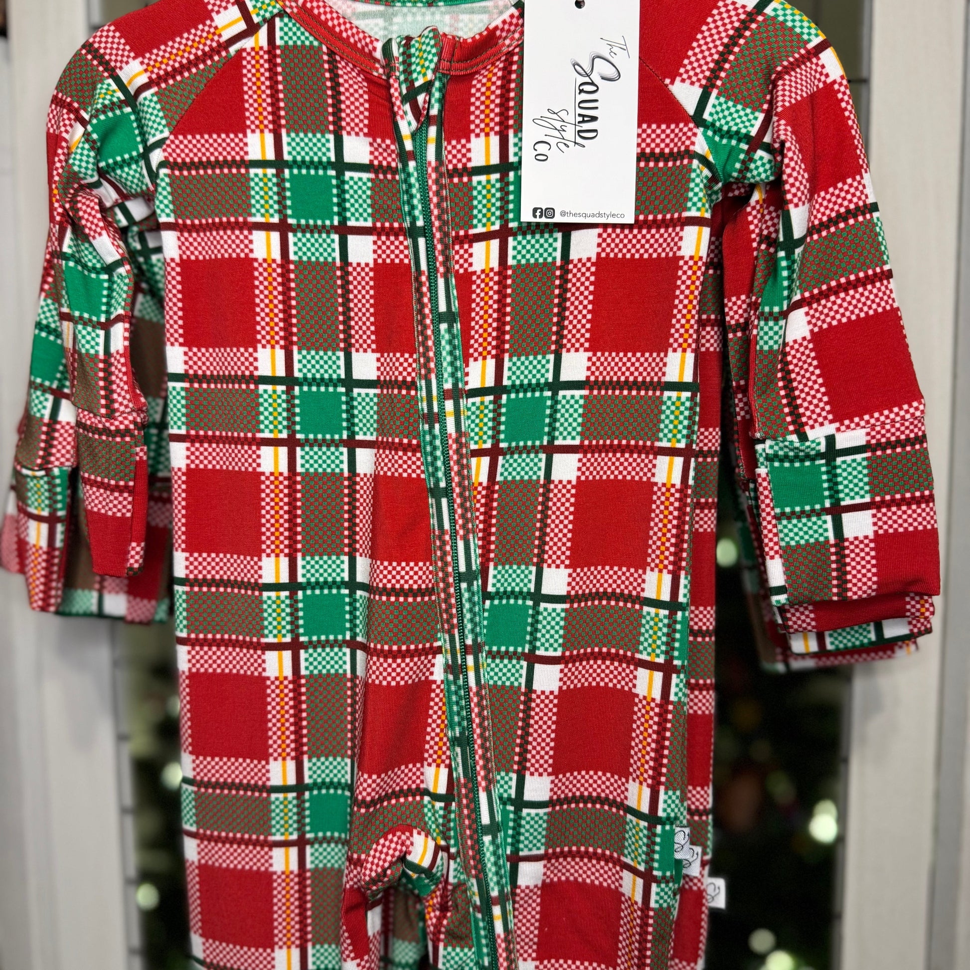 Plaid you're here convertible romper close up hanging in front of a Christmas tree.