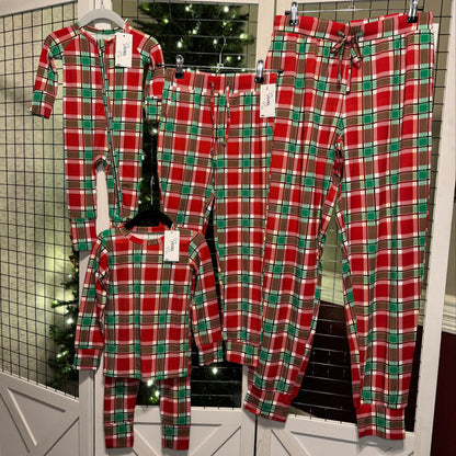 Plaid you're here family pajamas hanging in front of a Christmas tree.